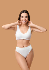 Smiling woman with perfect skin in underwear posing on beige background. Body care