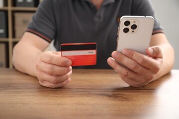 Man with credit card and smartphone at wooden table indoors, closeup