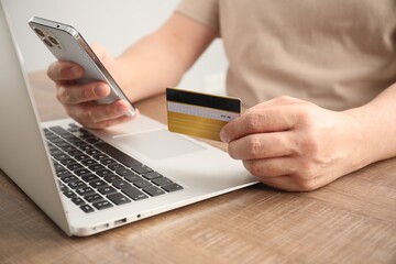 Man with credit card and smartphone at wooden table indoors, closeup