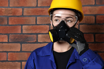 Worker in respirator, protective glasses and helmet near brick wall