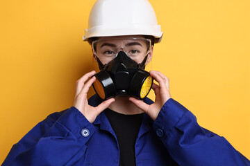 Worker in respirator, protective glasses and helmet on orange background