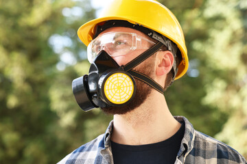 Man in respirator mask and hard hat outdoors. Safety equipment