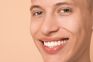 Happy young man on beige background, closeup. Dental veneers