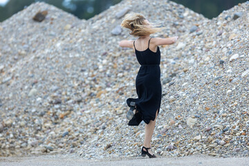 Young beautiful woman in black dress and sand quarry background, in motion