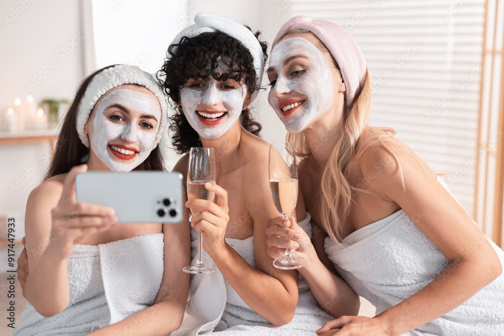 Wall mural Happy friends with facial masks and glasses of sparkling wine taking selfie in bathroom. Spa party