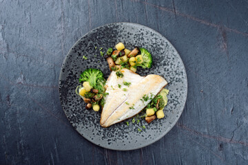 Fried cod fillet with baby king oyster mushrooms, broccoli and gnocchi served on mashed potatoes as top view on a rustic design plate with text space