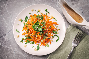 Carrot and parsley salad with Vinaigrette sauce on a white plate on a gray background. A place to copy the space.