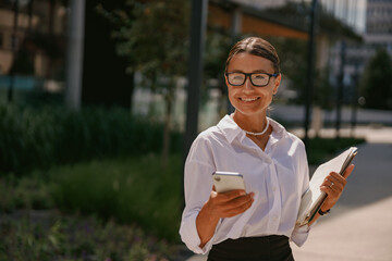 A professional woman is actively engaged with her smartphone while situated in an urban environment