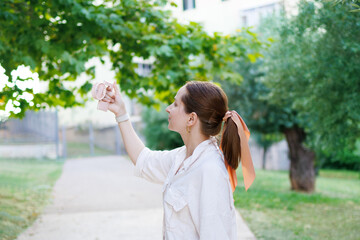 Obraz premium Young Brunette 32's Aged Woman Holding Handheld Fan In Hand That Blowing To Her Face On Garden Background. Portable Fan. Summer Device. Climatic Change. Small Ventilator