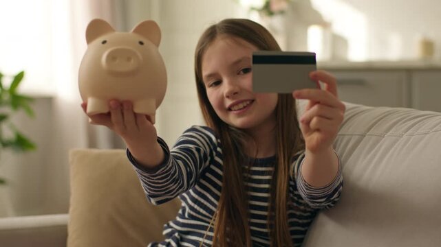 Happy little girl show at camera piggy bank credit debit card banking money finance smiling budget cash shopping saving calculating capital currency pay transaction child female kid daughter economy
