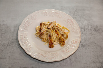 Fettuccine Alfredo with chicken topped with grated parmesan cheese served on a plate.