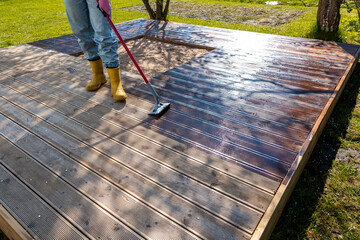 Applying stain to a wooden deck with a brush on a sunny day