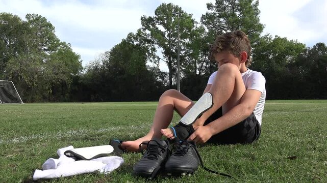 Low angle shot of a little boy soccer player putting on his shin guards before a match or a practice session