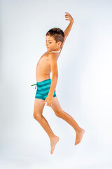 Energetic young boy in striped swim trunks jumping joyfully in the air, arms out wide and feet off...