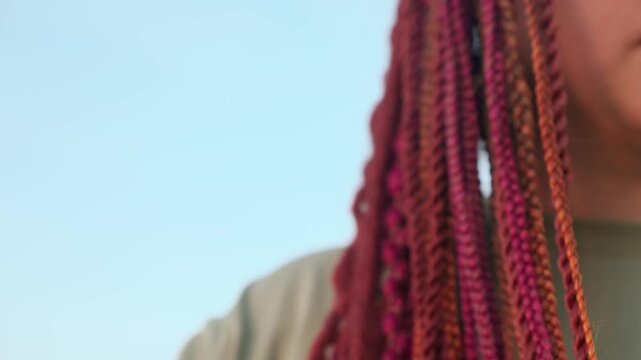 Beautiful young woman hairstyle with colorful hair extensions braid in thin braids and afro braids. Red dreadlocks close up