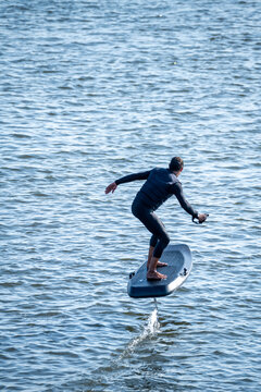Surfer balances on electric hydrofoil board, gliding above rippling water with arms outstretched