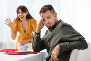 Bad date. Embarrassed man ignoring smiling woman indoors, selective focus