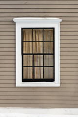 The exterior wall of a beige coloured building is made of narrow horizontal wooden clapboard.  There's a single hung closed block glass window with white crown trim molding and black glass dividers.