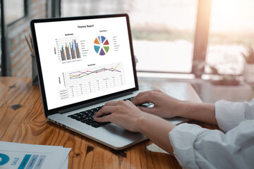 Hands typing on a laptop displaying financial graphs and charts, illustrating data analysis in a contemporary office environment.