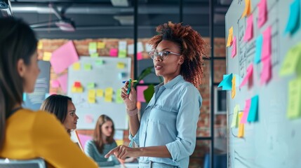 A confident businesswoman pointing at a whiteboard during a strategy meeting, with team members collaborating in the background. Ideal for themes of leadership, teamwork, and business strategy.
