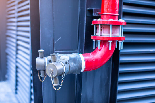 Outdoor fire department connection Siamese twin inlet valve connected to a bright red water pipe system on an industrial building exterior.