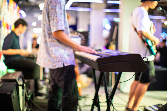 Side view of a live band performing with a focus on the keyboardist, guitarist, and drummer in a blurry background.