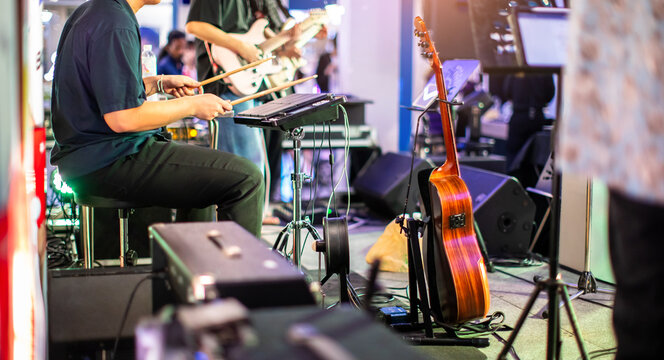 Musician playing electronic sample pad controller with guitarists performing on stage during a live band concert.