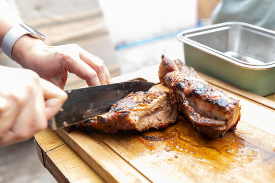 hands of a person cutting a juicy piece of meat on wooden board outdoors using a smartwatch. Celebrating Chile's national holidays where people eat meat to celebrate