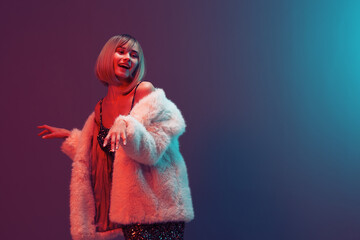 Dancing smiling adorable blonde woman in fluffy fur coat sparkly dress look aside posing isolated in blue turquoise red color light studio background. Neon party Fashion concept. Copy space Banner