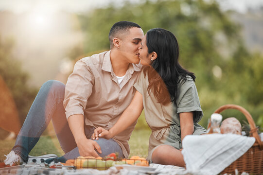 Kiss, nature and couple on picnic for summer date on vacation, getaway or weekend trip. Love, fruit and young man and woman with connection, bonding and marriage honeymoon holiday in outdoor park.