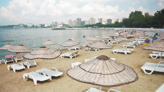 People resting on the Caddebostan sandy beach. Citizens swimming and sunbathing under umbrellas on summer sunny day. Asian side of Istanbul city in the background