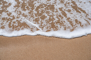 Texture of a wave from the sea with a little white foam slowly advancing a sandy beach