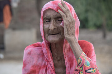 A helpless elderly woman with a sad, pained expression sits in a refugee camp