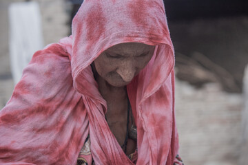 A helpless elderly woman with a sad, pained expression sits in a refugee camp