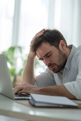 A stressed man sitting at a desk with a laptop, holding his head in frustration, representing the challenges of work-related stress in a modern setting.