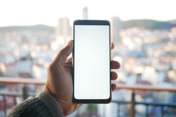 A Hand Gripping a Smartphone Set Against a Stunning Cityscape Background in Daylight