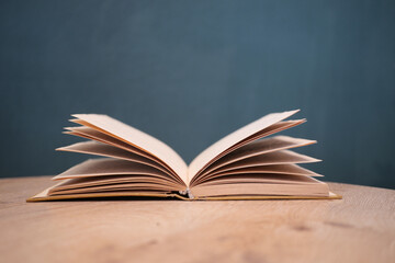 An open book with its pages gently turning rests on a wooden table in the breeze