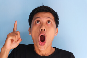 Shocked face of young Asian man pointing up in black t-shirt