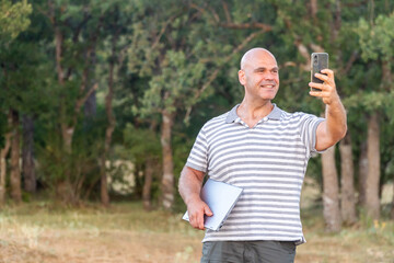 Standing man working in nature with a laptop and a phone, digital nomad concept