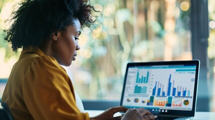 A black woman examining financial information on a laptop in a blended office environment for digital business performance tracking.