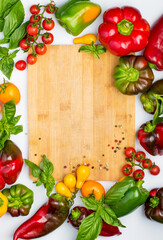 Multi-colored bell peppers, cherry tomatoes, basil sprigs and a board on a white background. Top view, copy space. Healthy nutrition concept.