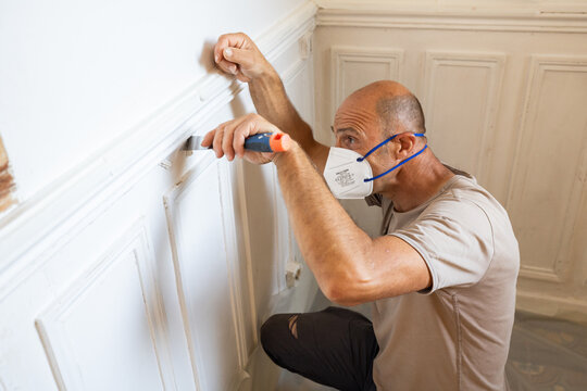 Illustration de l'utilisation d'une spatule pour retirer du pl&acirc;tre et de la peinture sur une cimaise en bois.