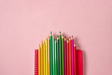 Arrangement pencils in red green yellow colours and red notebook on pink background. Art school concept