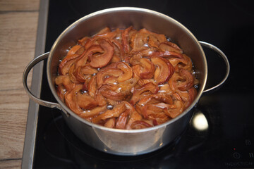 Pot of simmering apple slices on induction cooktop. Kitchen countertop with stove and cooking ingredients