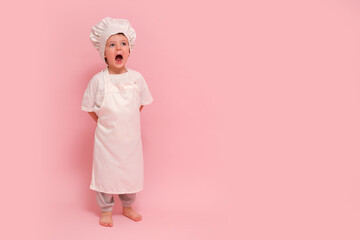 Child dressed as a chef in white uniform, studio portrait on pink background. Cooking and culinary concept, full-length photography. Kid aged 3 years (three year old boy)