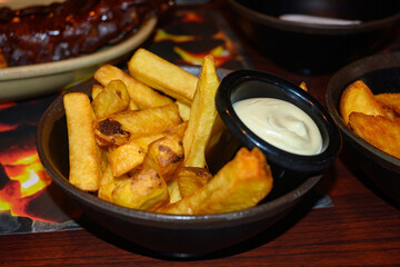 Close up photo of a bowl of golden Belgian fries with a jar of sauce (mayonnaise) on the table.