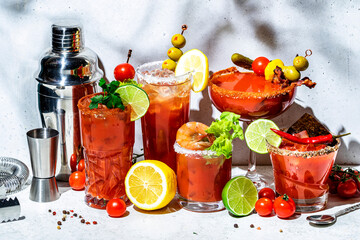 Tomato juice and vodka alcoholic cocktails with hot sauce, salt, pepper, olives and celery. Cocktail party. Gray background, hard light