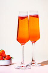 Strawberry festive cocktail drink with dry champagne, fruit puree and ice in glasses. Beige pink background, hard light