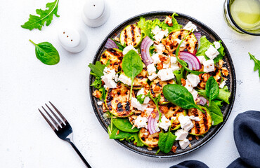 Summer grill salad with zucchini, feta cheese, nuts, onion, arugula and spinach on white background, top view