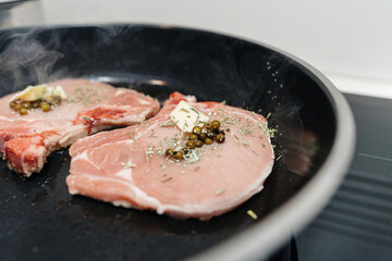 Pork steaks are seasoned with delicious herbs, green mustard, and butter, sizzling in a pan as they prepare for a tasty lunch or dinner at home, showcasing a mouthwatering homemade meal